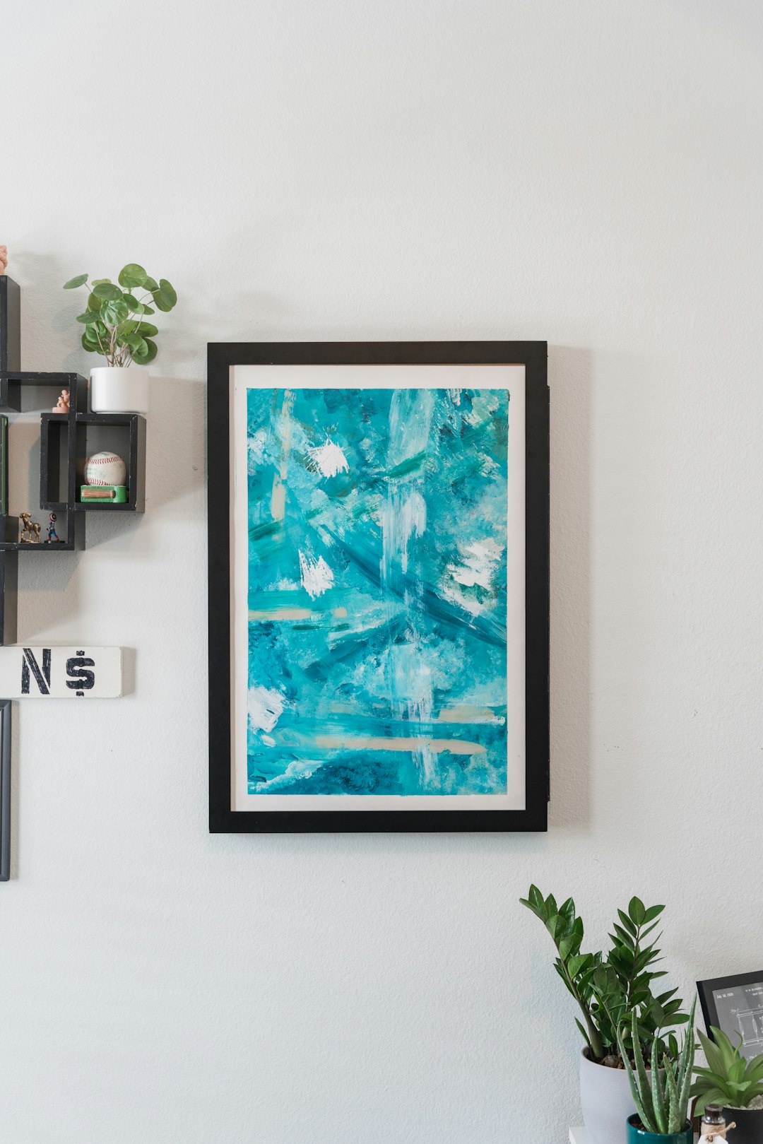: Immerse yourself in the beauty of a blue abstract wall art surrounded by decorative elements and table plants, creating a harmonious and artistic atmosphere.