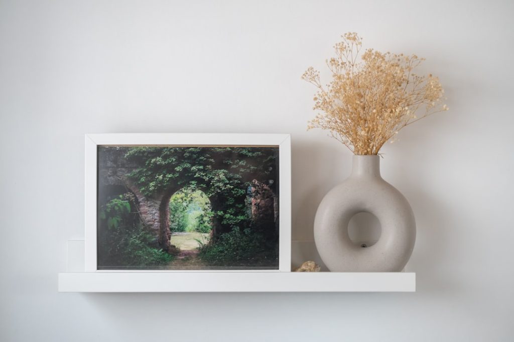 framed-artwork-of-a-garden-archway-next-to-a-vase-gx-eytaplse